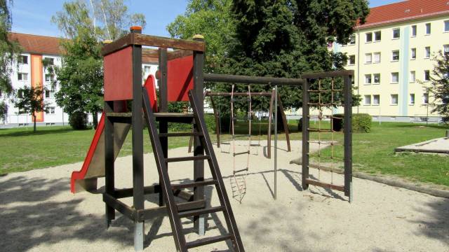 Spielplatz in dunklem Holz mit roter Rutsche, sowie Schaukel