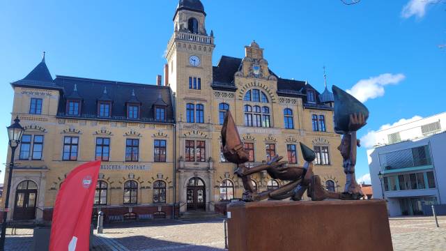 Fotopunkt  Historisches Rathaus in Bad Lausick mit moderner Skulptur und roter Info-Fahne – einladender Fotopoint am sonnigen Marktplatz.